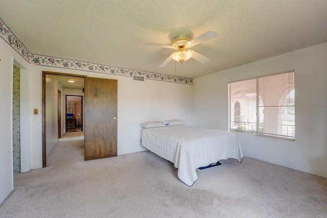 bedroom featuring visible vents, light carpet, a textured ceiling, and a ceiling fan