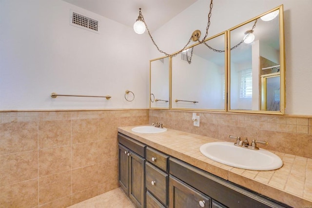 full bathroom with a sink, visible vents, tile walls, and double vanity