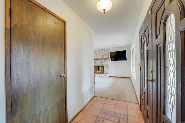 entryway with visible vents, baseboards, light tile patterned flooring, a fireplace, and light colored carpet