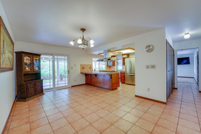 kitchen with a peninsula, light tile patterned floors, freestanding refrigerator, and island range hood