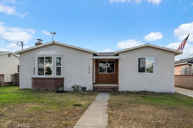 view of front of house featuring fence, a chimney, stucco siding, a front lawn, and brick siding