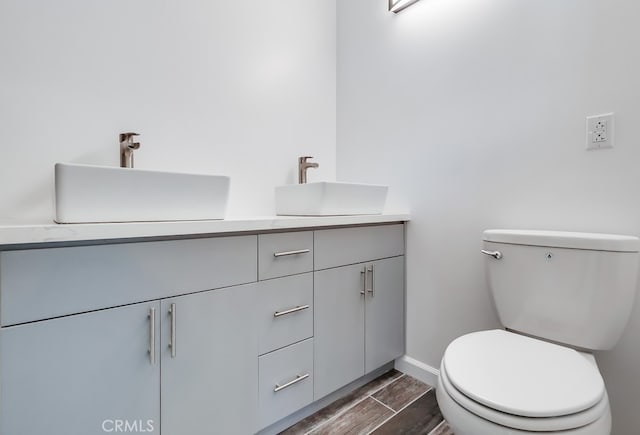 bathroom featuring double vanity, wood finish floors, toilet, and a sink