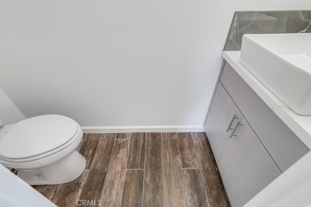 half bath with toilet, vanity, baseboards, and wood finished floors