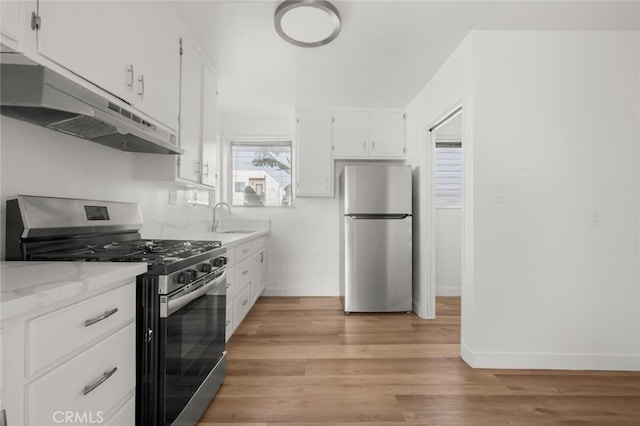 kitchen with under cabinet range hood, a sink, stainless steel appliances, white cabinets, and light wood finished floors