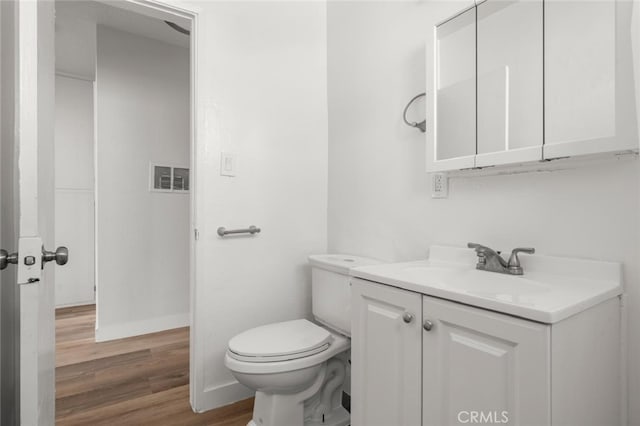 half bath with visible vents, toilet, wood finished floors, and vanity