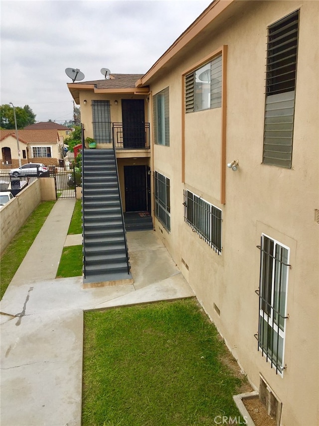 rear view of property featuring crawl space, stairway, stucco siding, and fence