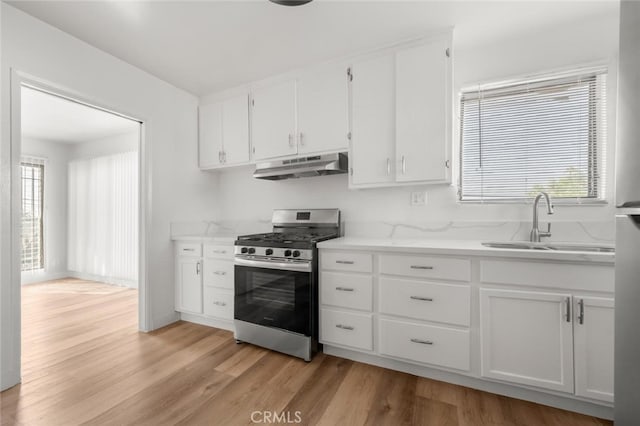 kitchen with under cabinet range hood, stainless steel range with gas stovetop, light wood-style floors, and a sink