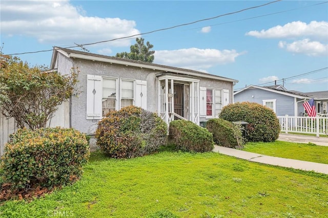 bungalow featuring stucco siding, a front lawn, and fence