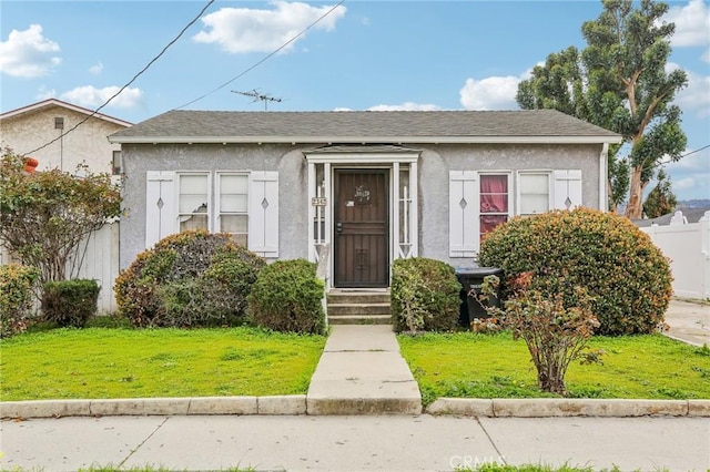 bungalow-style home with stucco siding, a front lawn, and fence