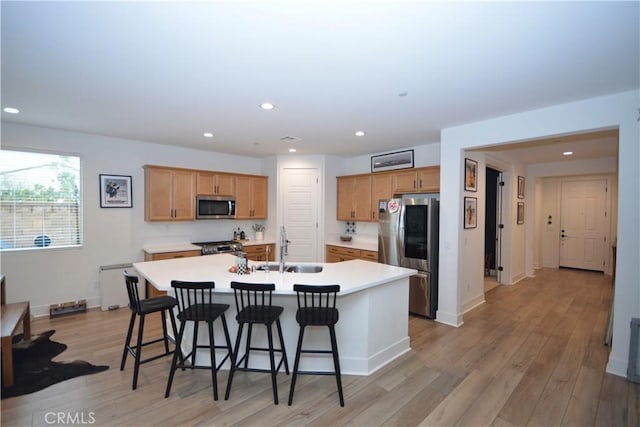 kitchen featuring a sink, a kitchen bar, light wood-type flooring, stainless steel appliances, and a kitchen island with sink