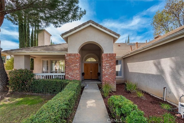 entrance to property with a porch, a chimney, stucco siding, a tiled roof, and brick siding