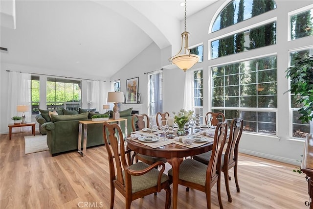 dining space featuring baseboards, arched walkways, light wood-type flooring, and high vaulted ceiling