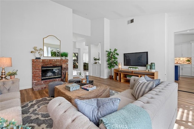 living area featuring a brick fireplace, wood finished floors, visible vents, and a towering ceiling