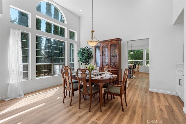 dining space with baseboards, light wood-style flooring, and a towering ceiling