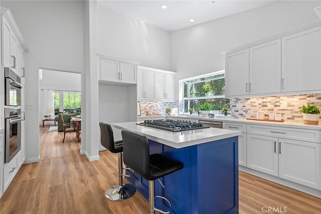 kitchen featuring a center island, a breakfast bar, a towering ceiling, white cabinets, and gas cooktop