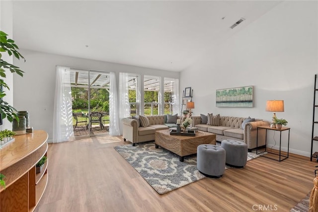 living area featuring a high ceiling, wood finished floors, visible vents, and baseboards