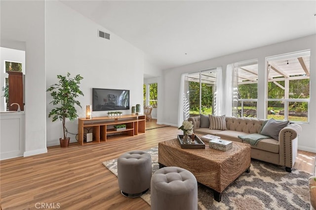 living area with high vaulted ceiling, wood finished floors, visible vents, and baseboards