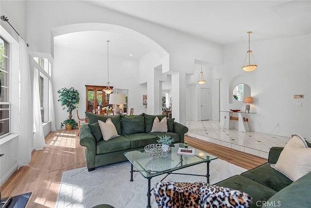 living area featuring arched walkways, light wood-type flooring, and a high ceiling