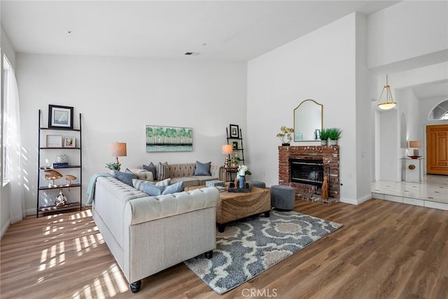 living room with visible vents, wood finished floors, a fireplace, baseboards, and a towering ceiling