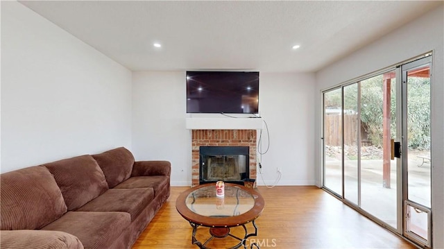 living area featuring recessed lighting, baseboards, a brick fireplace, and light wood finished floors