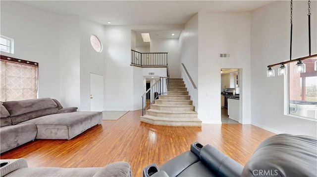 living room with visible vents, baseboards, stairway, a towering ceiling, and wood finished floors