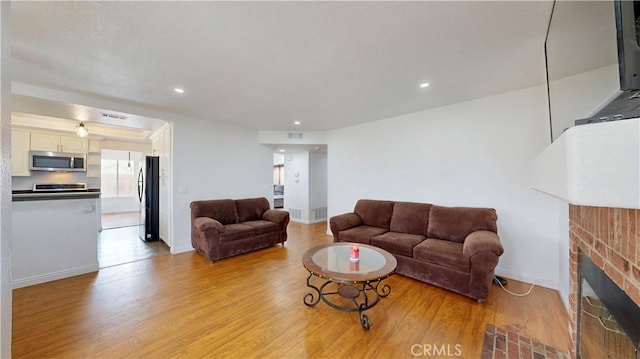 living area with visible vents, a brick fireplace, baseboards, light wood-type flooring, and recessed lighting