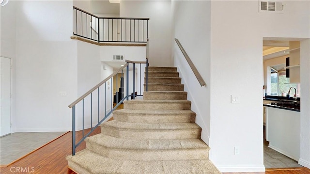 stairs with a high ceiling, wood finished floors, visible vents, and baseboards