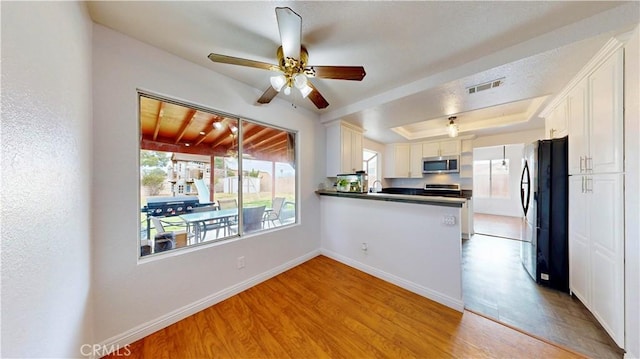 kitchen featuring stainless steel microwave, visible vents, a tray ceiling, light wood-style flooring, and freestanding refrigerator