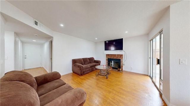 living area with visible vents, baseboards, recessed lighting, a brick fireplace, and light wood-type flooring