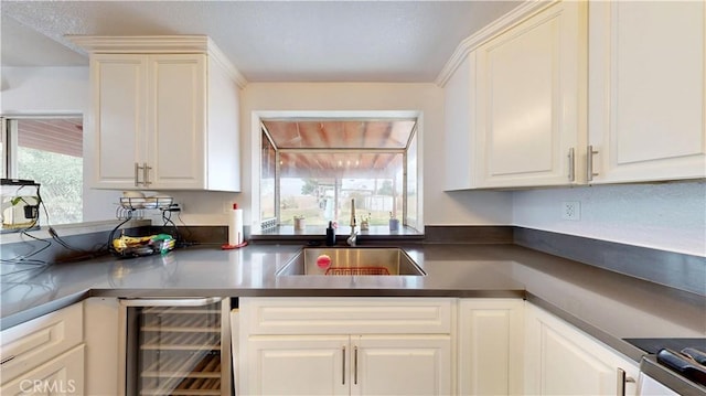 kitchen with dark countertops, wine cooler, white cabinets, and a sink