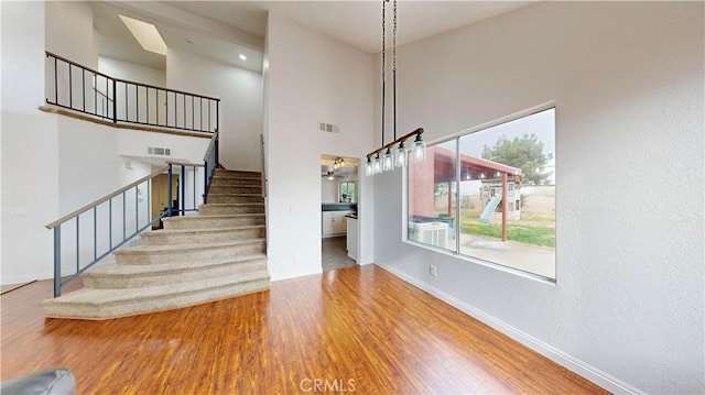 stairs featuring visible vents, a towering ceiling, baseboards, and wood finished floors