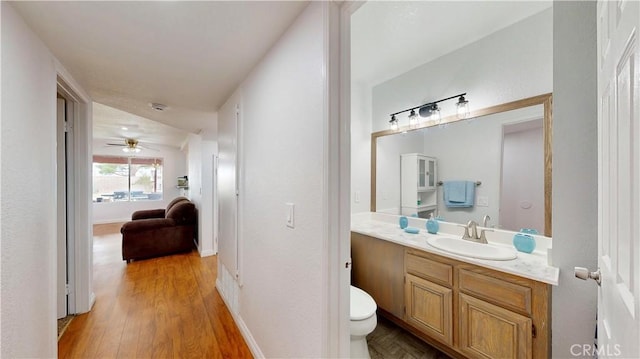 half bath featuring baseboards, toilet, wood finished floors, vanity, and a ceiling fan