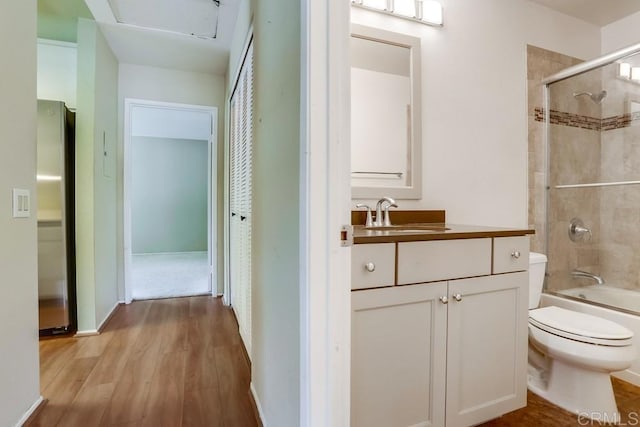 full bath featuring bath / shower combo with glass door, toilet, vanity, and wood finished floors