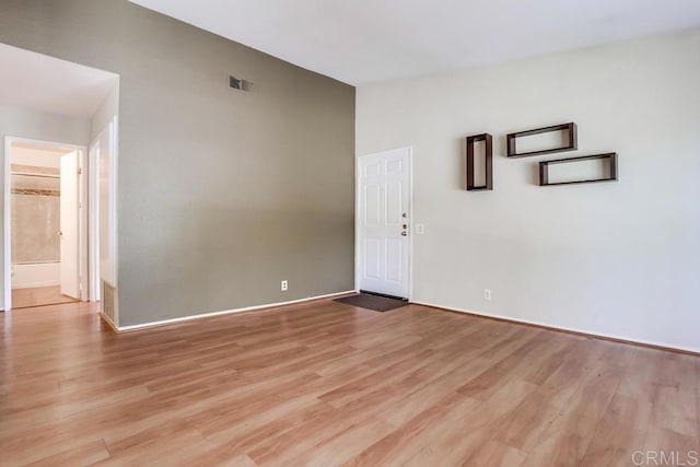 empty room featuring light wood finished floors, visible vents, and lofted ceiling