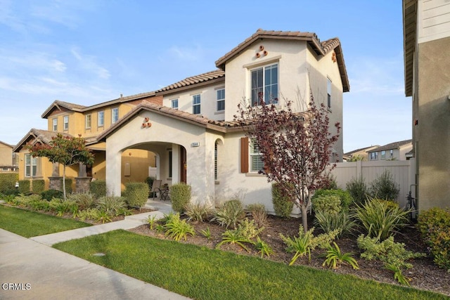 mediterranean / spanish-style house featuring a tile roof, fence, and stucco siding