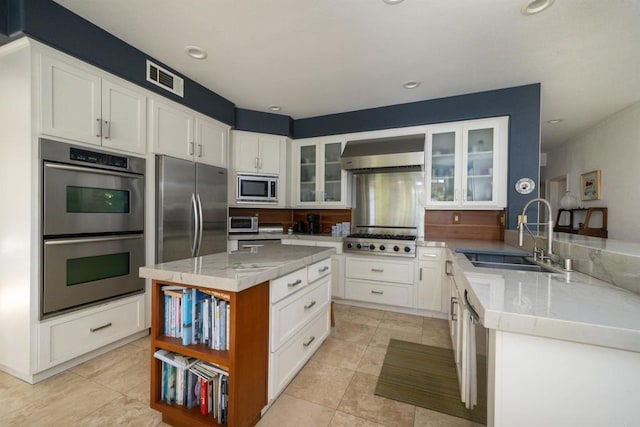 kitchen featuring visible vents, a sink, appliances with stainless steel finishes, white cabinets, and wall chimney range hood