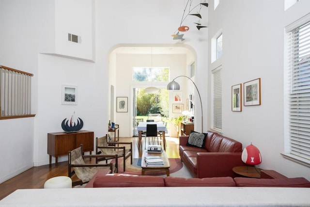 living room with wood finished floors, baseboards, visible vents, a high ceiling, and arched walkways