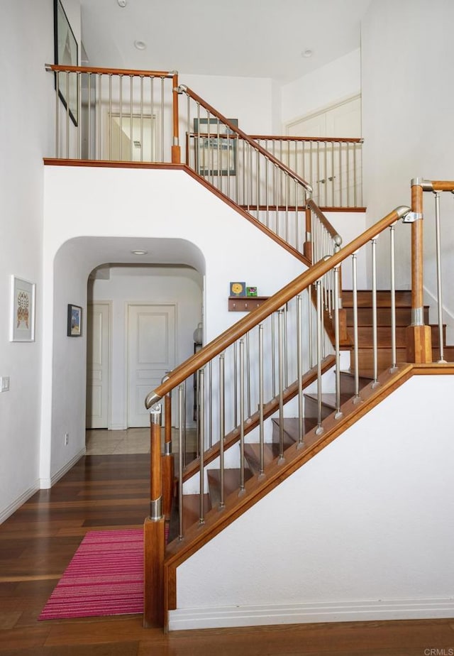 stairs with baseboards, wood finished floors, arched walkways, and a towering ceiling