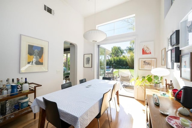 dining area with arched walkways, visible vents, a high ceiling, and wood finished floors