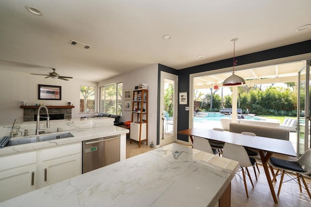 kitchen with visible vents, light stone counters, stainless steel dishwasher, white cabinets, and a sink