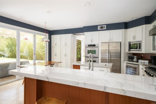 kitchen featuring light stone counters, beverage cooler, visible vents, stainless steel appliances, and pendant lighting