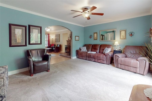 living area with baseboards, arched walkways, ceiling fan, ornamental molding, and carpet flooring