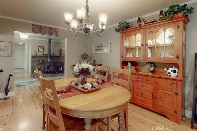 dining space with a chandelier, light wood-style flooring, crown molding, and a wood stove