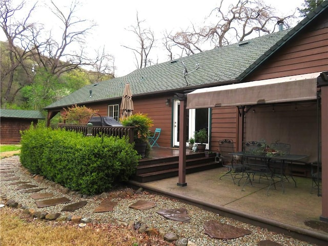 back of house with a wooden deck, roof with shingles, and a patio area