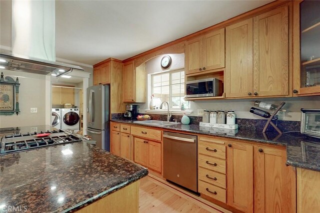 kitchen with a sink, island exhaust hood, washing machine and dryer, appliances with stainless steel finishes, and glass insert cabinets