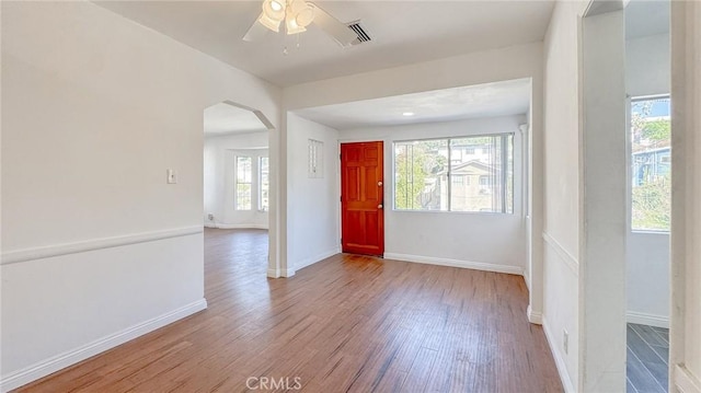 spare room featuring visible vents, arched walkways, baseboards, and wood finished floors