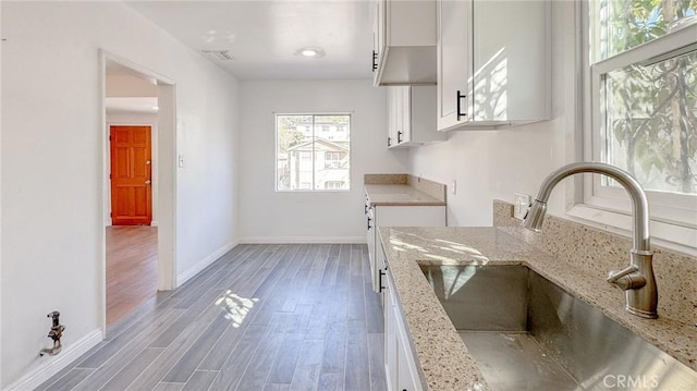 kitchen with white cabinetry, wood finished floors, light stone countertops, and a sink