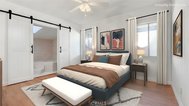 bedroom featuring a barn door, connected bathroom, light wood-style floors, baseboards, and ceiling fan