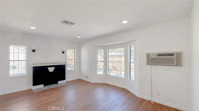 unfurnished living room with baseboards, a wall unit AC, and wood finished floors