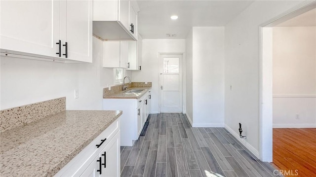 kitchen featuring wood finish floors, a sink, white cabinets, baseboards, and light stone countertops